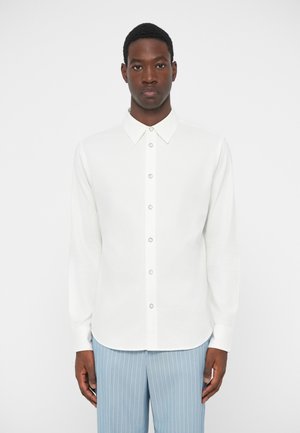 Chemise blanche à manches longues avec col pointu, fermeture à boutons à l'avant et texture lisse. Associée à un pantalon à rayures verticales bleu clair.
