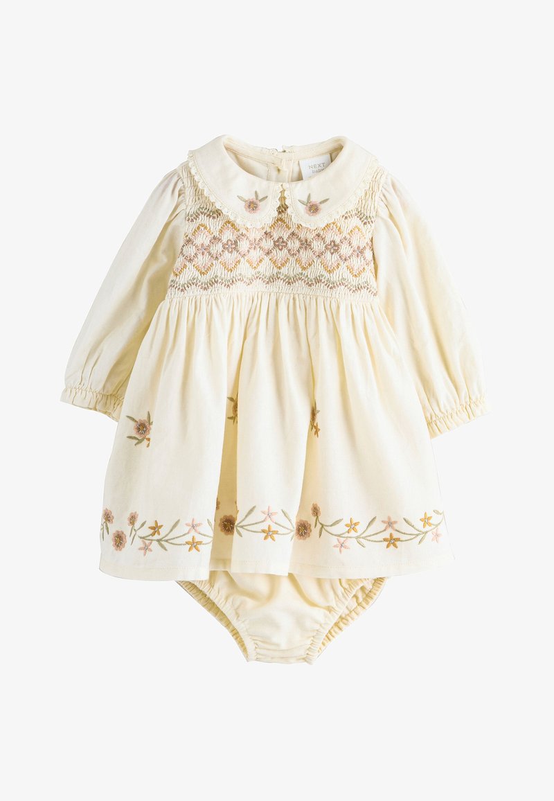 Vestido de bebé de manga larga en color crema con fruncido floral, flores bordadas en el bajo, cuello con borde festoneado y pantalones cortos tipo bloomers a juego debajo.