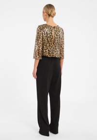 Haut en imprimé léopard à sequins avec des manches trois-quarts, présentant une ouverture en keyhole au dos. Assorti à un pantalon noir ample.