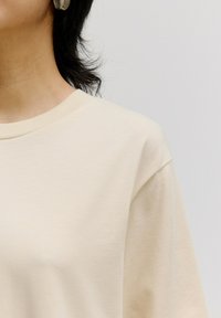 Beige T-shirt met korte mouwen en een ronde hals. Zacht, glad materiaal met een relaxed fit en subtiele stiksels op de mouwen.