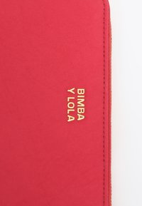 Pañuelo de tela roja con una textura suave, letras doradas que dicen "BIMBA Y LOLA", con bordes cosidos para mayor durabilidad.