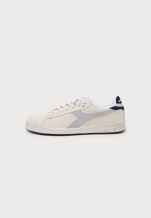 Low-top beige leather sneaker with gray suede side detail, white inner lining, and textured sole with black bottom.
