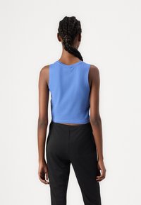 Lühike, varrukateta topp helesinises kangas, millel on ümar kaelus, koos mustade pükstega. Sile tekstuur, igapäevane disain.