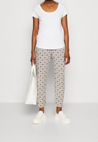 Valkoinen lyhytnukkasa paita on yhdistetty kuviollisiin vaaleanharmaisiin housuihin, joissa on punaisia ja sinisiä kuvioita, sekä valkoisiin tennareihin, mukana valkoinen kassi.