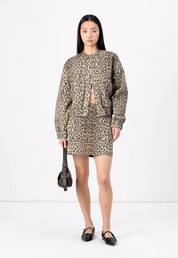 Leopardmönstrad kort jacka och matchande minikjol; texturerad tyg; neutrala toner med mörkare fläckar; paret med en liten väska och platta skor.