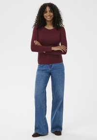 Maroon long-sleeve top paired with light blue wide-leg jeans and brown shoes, featuring a round neck and textured fabric.