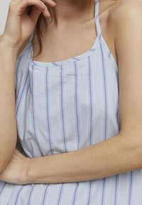 Ljust blå ärmlös topp med vertikala ränder i nyanser av blått och vitt, tillverkad av mjukt material med avslappnad passform och subtil struktur.