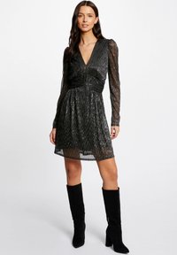 Zwarte jurk met lange doorzichtige mouwen, gerimpelde lijf en textiel stof. Gepaard met zwarte suede laarzen tot de knie.
