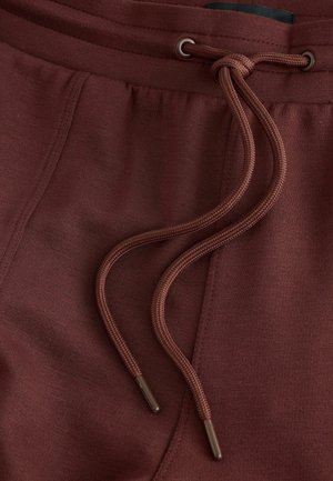 Bordeauxrøde joggingbukser med en glat tekstur, der har en elastisk talje, snøre med metalender og sidelommer for funktionalitet.