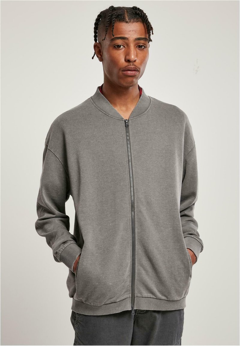 Grå zip-upp sweatshirt med ribbad krage, långa ärmar och sidofickor, tillverkad av mjukt tyg med en slät yta.