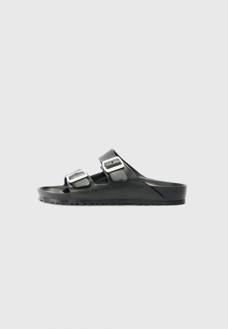 Sandal nera con slip-on, dotata di due fibbie regolabili in argento e suola testurizzata, mostrata di lato su uno sfondo chiaro e semplice.