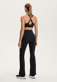 Fekete sportmelltartó kulcslyuk hátkialakítással, magas derékkal ellátott fekete, harangszárú leggings-szel párosítva. Simogató, rugalmas anyag. Fekete sportcipők.