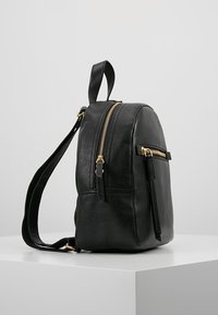 Schwarzer Leder-Rucksack mit runder Form, goldenen Reißverschlussakzenten und einer Fronttasche. Verfügt über einen einzigen Tragegurt und eine strukturierte Oberfläche.