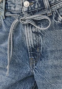 Pantaloni din denim într-un albastru estompat, cu un șnur la talie, având un nasture metalic, cusături contrastante și o croială lejeră și relaxată.