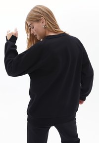 Felpa nera a collo rotondo con una vestibilità rilassata, dotata di maniche lunghe e polsini a costine. Il materiale sembra morbido e presenta un design pulito e semplice.