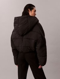 Svart puffjakke med hette, har en quiltet design og en overdimensjonert passform, laget av lett materiale. Kjent for sin glatte tekstur.