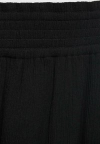 Black elasticated waistband with gathered texture, featuring fine stitching details. Material appears soft and fluid in design.