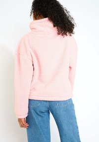 Pullover in pile rosa soffice, con colletto alto, maniche lunghe e vestibilità rilassata. La vista posteriore rivela dettagli di cucitura e texture.