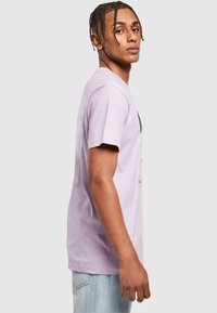 Light lavender cotton t-shirt with short sleeves and a relaxed fit. Features a simple graphic design on the front. Soft texture, casual style.