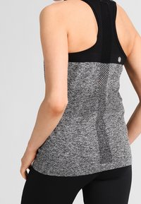 Top sportivo grigio mélange con spalline incrociate, yoke in rete nera e pannello posteriore in tessuto testurizzato. Presenta un piccolo logo decorativo.