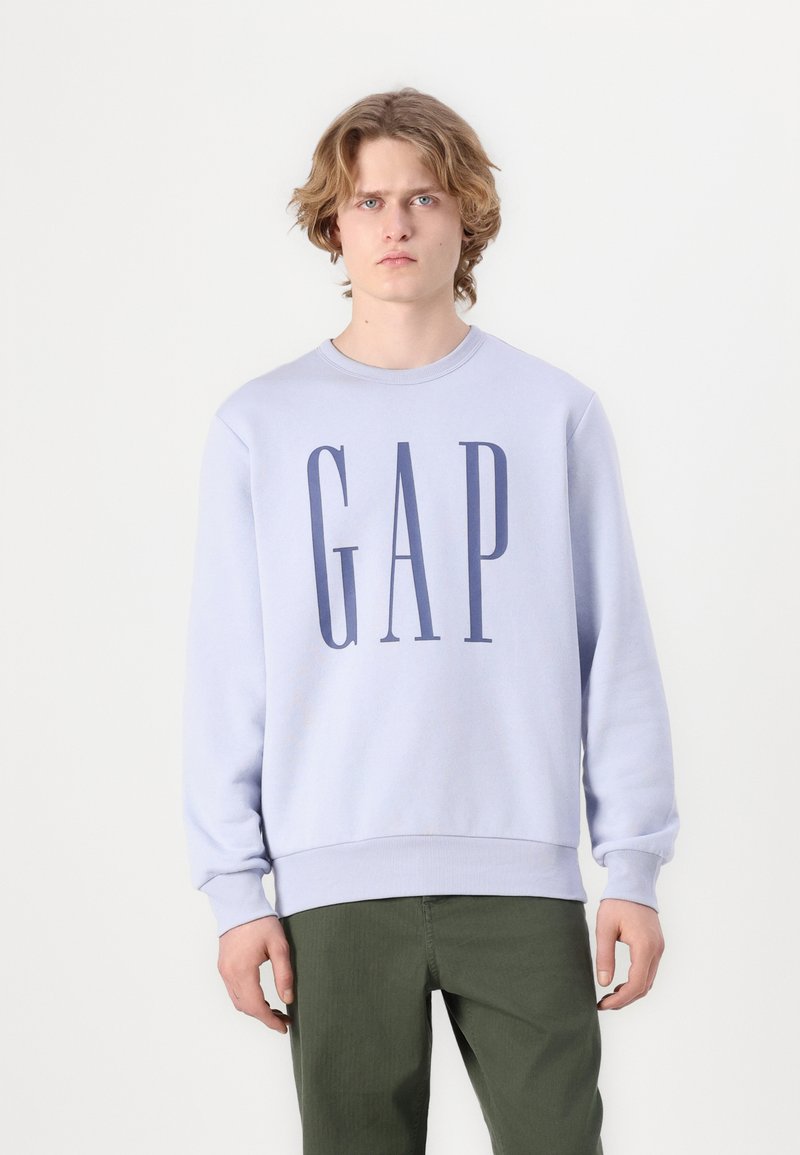 Ανοιχτό μωβ φούτερ με μεγάλο ναυτικό λογότυπο "GAP" μπροστά. Διαθέτει στρογγυλή λαιμόκοψη και ριμπ μανσέτες. Φοριέται με πράσινα παντελόνια.