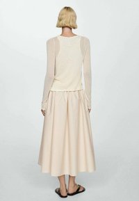 Blusa de manga larga y ligera en crema con textura transparente, combinada con una falda rosa pálido hasta la rodilla, que presenta una cintura fruncida y una tela suave.