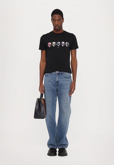 Svart bomull t-shirt med tecknade ansikten i flera färger; parat med blå denimjeans och en svart väska med färgade accenter.