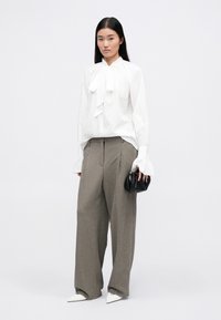 Blusa bianca con un dettaglio a fiocco e maniche ampie, abbinata a pantaloni grigi a vita alta e gamba larga e una piccola borsa nera.