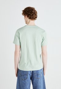 Camiseta de manga corta color verde menta, hecha de suave algodón, con un clásico cuello redondo, combinada con unos pantalones cortos de mezclilla azul de corte suelto.