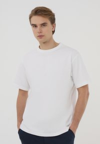 T-shirt bianca in cotone con maniche corte, scollatura a crew e vestibilità comoda. Design minimalista senza motivi o dettagli visibili.