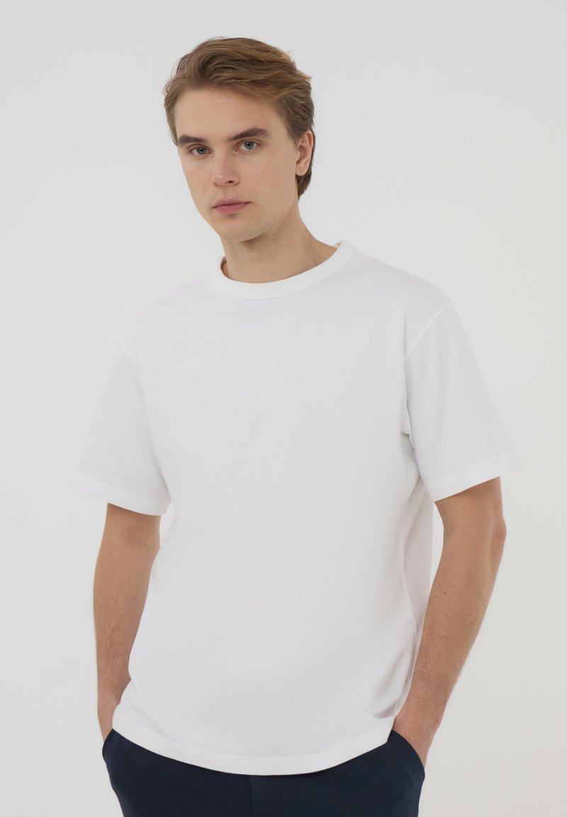 T-shirt bianca in cotone con maniche corte, scollatura a crew e vestibilità comoda. Design minimalista senza motivi o dettagli visibili.