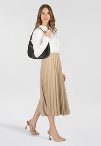 Gonna midi beige plissettata, camicia bianca con bottoni e décolleté nude. Borsa in pelle nera con dettagli di logo discreti.