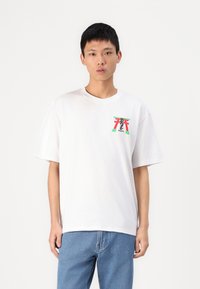 Tricou alb din bumbac, cu mâneci scurte, având un design grafic colorat în roșu, verde și negru pe piept. Croială casual.