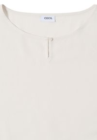 Blusa color crema con scollatura rotonda, chiusura con bottoni sotto il collo e una texture del tessuto liscia. Etichetta con scritto "CECIL."