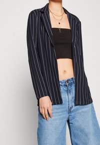 Námořnický pruhovaný blejzr s výstřihem na klopu, spárovaný s černým crop topem a modrými džíny s vysokým pasem, které mají pohodlný střih a denní texturu.