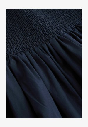 Granatowa sukienka z marszczonym stanem i marszczoną spódnicą. Gładka faktura tkaniny z równomiernie rozmieszczonymi plisami wzdłuż brzegu.