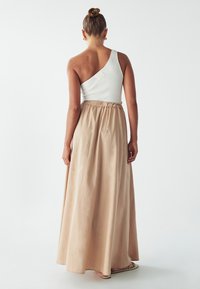 Abito lungo con parte superiore a spalla scoperta in jersey bianco a coste e gonna beige liscia con cintura elastica, in materiale fluido che arriva fino a terra.