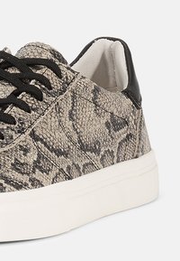 Sneaker z wierzchem w czarny i beżowy wzór węża, teksturowany materiał, czarne sznurówki i biała gumowa podeszwa. Posiada kontrastujący czarny obcas.