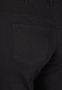 Čierne džínsy z denimu s jednou zadnou vreckom a jemným zakrivením. Materiál má matný povrch a viditeľné švy.