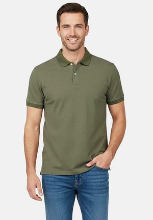 Olivengroen poloshirt met een kraag, voorzien van korte mouwen en twee knopen bij de hals. Draagt met een blauwe spijkerbroek.