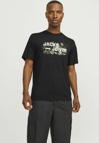 Juodas medvilnės marškinėliai su maskuojančiu raštu, ant kurių ryškiomis baltomis raidėmis užrašyta "JACK & JONES". Trumpomis rankovėmis ir standartinio kirpimo.