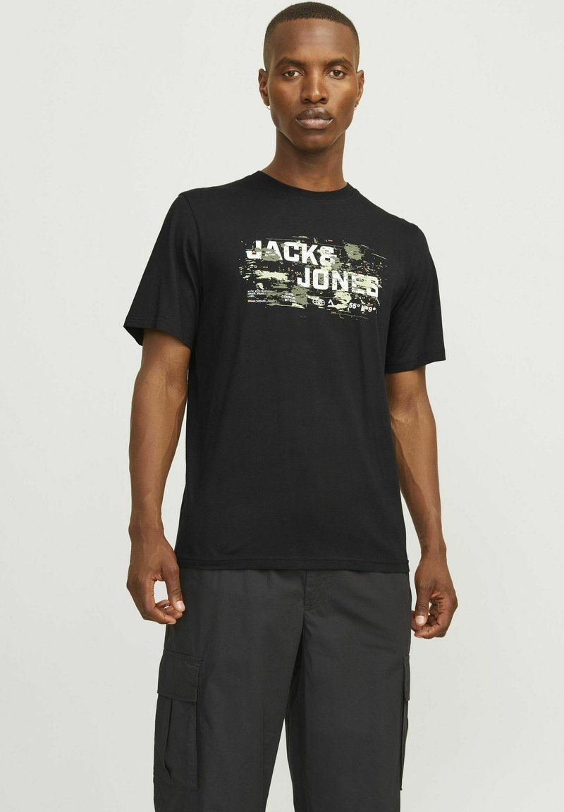 Juodas medvilnės marškinėliai su maskuojančiu raštu, ant kurių ryškiomis baltomis raidėmis užrašyta "JACK & JONES". Trumpomis rankovėmis ir standartinio kirpimo.
