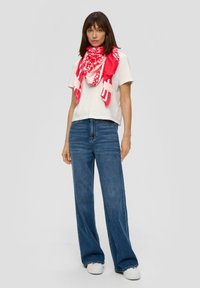 T-shirt blanc à manches courtes, jeans taille haute bleu, coupe oversize, accompagné d'un foulard rose à motifs et de baskets blanches.