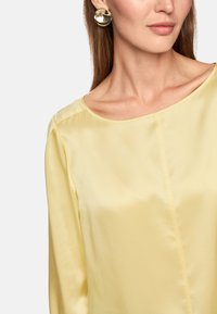 Silk yellow blouse with a round neckline and subtle sheen, paired with large circular gold earrings. Soft texture, relaxed fit.