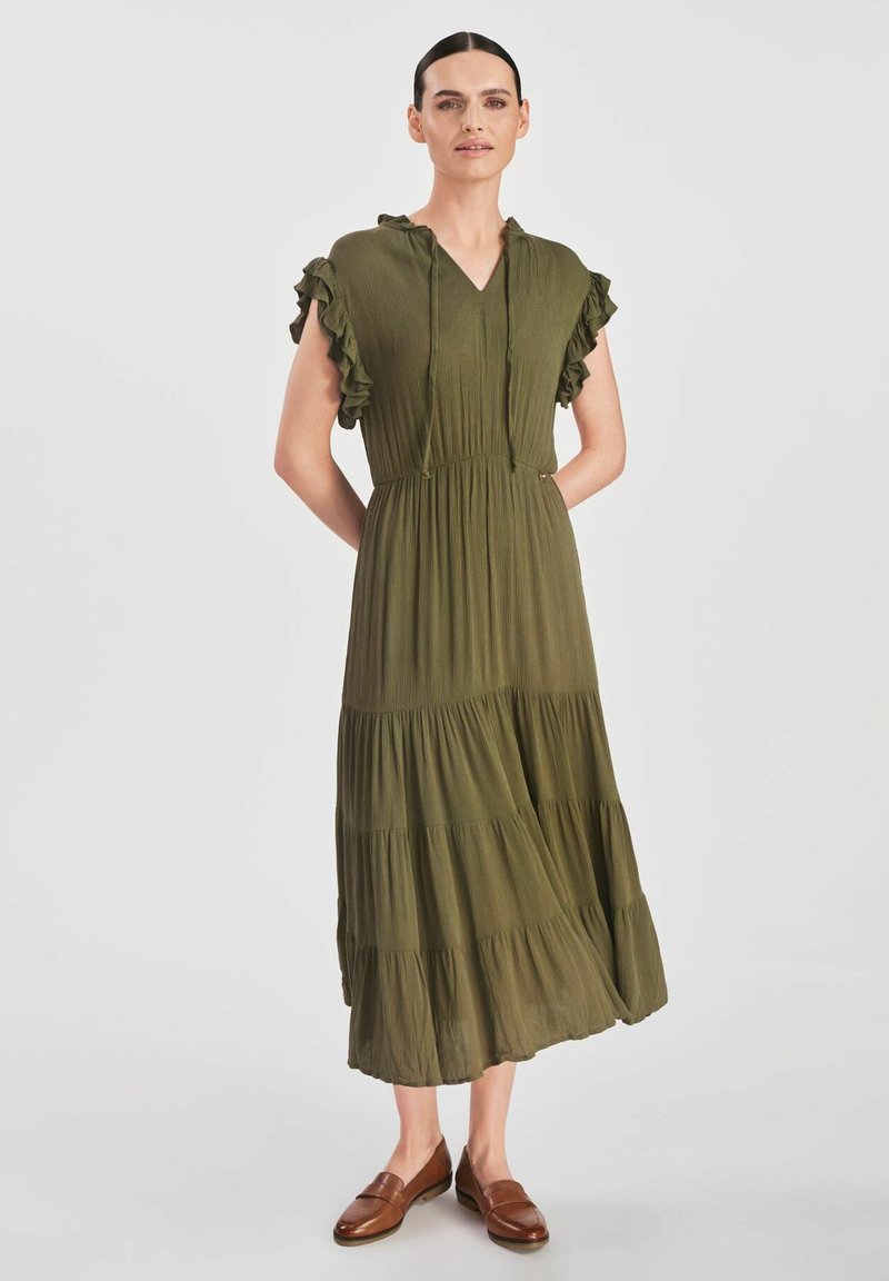 Oliwkowa sukienka z falbanami na krótkich rękawach, dekoltem w kształcie litery V i warstwową spódnicą. Wykonana z lekkiego materiału, z elastycznym paskiem w talii, co zapewnia możliwość dopasowania.