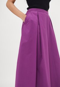 Falda plisada morada con bolsillos laterales, hecha de un material ligero con una textura suave, diseñada con una cintura alta.