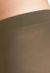 Olivgrüne Leggings mit einem strukturierten, gerippten Bund. Der Stoff ist glatt und weist ein dezentes geometrisches Muster auf.