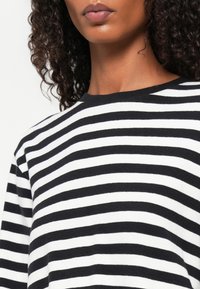 Zwart-wit gestreepte sweater met een ronde halslijn, lange mouwen en een textuur gebreide stof. De strepen variëren in breedte.