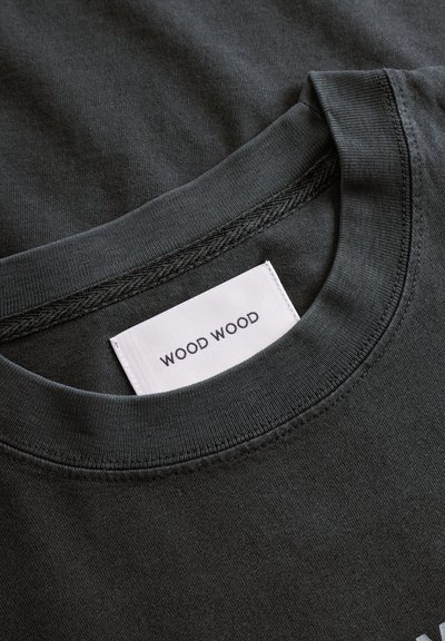 Tumši pelēkas krāsas kokvilnas t-krekls ar apaļu kakla izgriezumu un baltu etiķeti ar tekstu "WOOD WOOD", izšūtu iekšējā apkaklē.