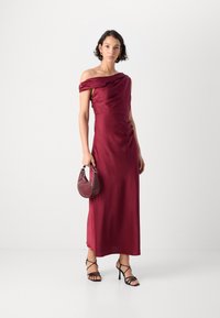 Bordo satino off-the-shoulder suknelė su prigludusia liemene, drapiruotu iškirpimu ir šoniniu išpjovimu. Papildyta mažąja tekstūruota rankine ir sagtimi sandalais.